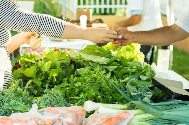person passing money over vegetables